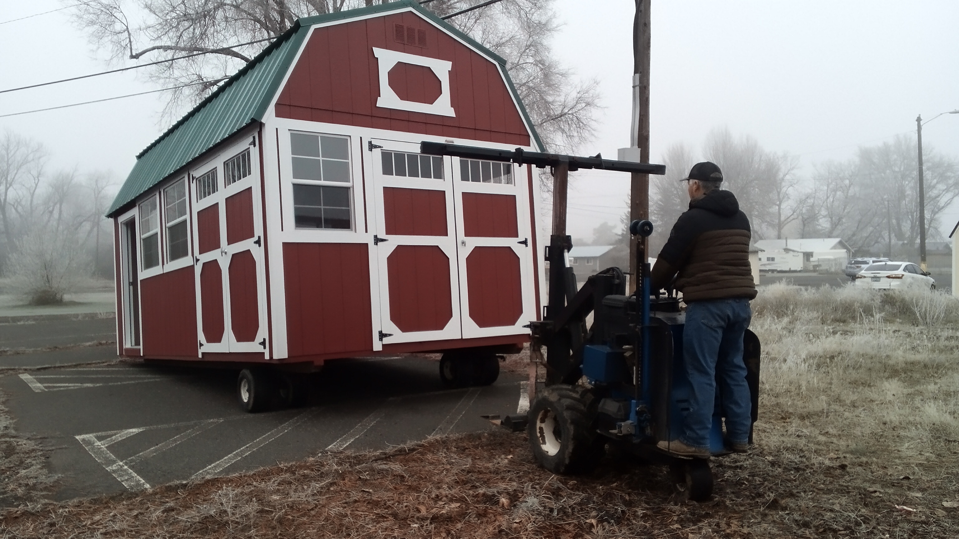 A person dressed in winter clothing on a fork lift lowers a red utility shed into place.