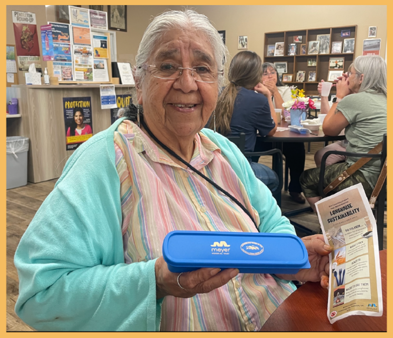 A woman holds a blue plastic box with gold images on it in one hand and an info graphic on a piece of paper in another.